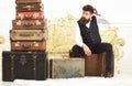 Luggage and relocation concept. Macho elegant on tired face sits, exhausted at end of packing, near pile of vintage