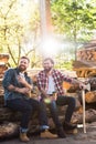 lumberjack with coffee cup pointing by finger to partner with axe sitting on logs