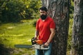 Lumberjack worker with chainsaw in the forest. Handsome young man with axe near forest. Stylish young man posing like Royalty Free Stock Photo