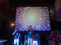 Luminaries rap on stage holding pointer finger in the air with trippy video show overhead