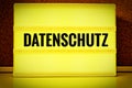 Luminous panel with the inscription in German Datenschutz in front of a pin board, in English Privacy Policy, in yellow with black