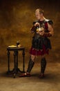 Portrait of medieval person, young man, warrior or knight in war equipment eating isolated on vintage dark background Royalty Free Stock Photo