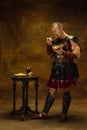 Portrait of medieval person, young man, warrior or knight in war equipment eating isolated on vintage dark background Royalty Free Stock Photo