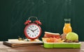 Lunch box with appetizing food and alarm clock on wooden table near green chalkboard Royalty Free Stock Photo