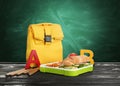 Lunch box with appetizing food and bag on table near green chalkboard Royalty Free Stock Photo