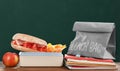 Lunch box with appetizing food and bag on wooden table near green chalkboard Royalty Free Stock Photo