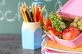 Lunch box with appetizing food and stationery on grey table near chalkboard Royalty Free Stock Photo