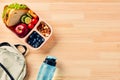 Lunch box with fruits, vegetables, sandwich, nuts, and backpack, water bottle on wooden table. Kids lunchbox for school dinner Royalty Free Stock Photo