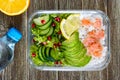 Lunch box: rice, salmon, salad with cucumber, avocado, greens, lemon, chia seeds and bottle of water on a wooden background. Royalty Free Stock Photo