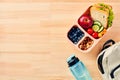 Lunch box with vegetables, fruits, sandwich, and bottle of water, and backpack on wooden table Royalty Free Stock Photo