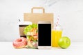 Lunch food set with coffee cup, orange juice, shrimp salad in plastic pack, apple, donut, packet, fruit, blank phone in white. Royalty Free Stock Photo