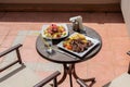 Lunch on the plate with lamb, potato and salad on the table outside on the balcony. Spring or summer blooming trees and flowers