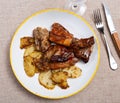 Lunch is served on plate - pieces of young rabbit baked with slice of potato. Close-up