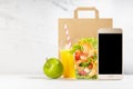 Lunch set with seafood salad with shrimps, orange juice, green apple, packet, blank phone in white interior. Mockup. Royalty Free Stock Photo