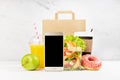 Lunch set of seafood shrimp salad in pack, orange juice, coffee cup, donut, packet, blank phone in white interior with marble tile Royalty Free Stock Photo