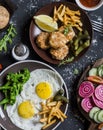 Lunch or snack table - fried eggs, chicken balls, potato chips, vegetables, sauces on a dark background. Rustic style, top view. Royalty Free Stock Photo