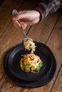 Lunch table - closeup male hand with italian spaghetti on vintage fork serving on black dishes. Pasta with vegetables, pepper, Royalty Free Stock Photo