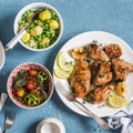 Lunch table. Lemon thyme baked chicken, boiled potatoes with green peas, salad with lentils and tomatoes on a blue background.