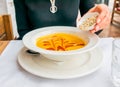 Lunch time, in front of a woman is a plate of lentil or pumpkin creme soup, in her hands is a small bowl with homemade crackers -