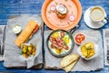 Lunch for two: frying pan with eggs and bacon, potatoes, sandwich, sauce and coffee, cutlery, on a blue denim background Royalty Free Stock Photo