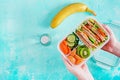Lunchbox in hands. School lunch box with sandwich, vegetables, water, and fruits on table. Healthy eating habits concept. Flat lay Royalty Free Stock Photo