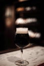 Luscious dark beer in an elegant glass, standing tall on the bar counter. Warm ambiance.