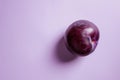 A ripe purple plum perched upon a soft, light purple backdrop