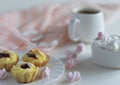 lush fruit sponge cakes with almonds on a white saucer, mini marshmallows in a china cup and a strong cup of coffee