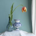 Lush natural light old Dutch Delft blue lidded vase with orange tulip  on  white linen against a blue background Royalty Free Stock Photo