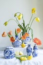 A Lush natural light stillife with old Dutch Delft blue lidded vase with yellow and orange tulips a gerbera and lemons on white Royalty Free Stock Photo