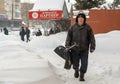 Lutsk, Ukraine - February 12,2020: An elderly man with snow shovel in winter. City street after blizzard. People walk in
