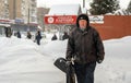 Lutsk, Ukraine - February 12,2020: An elderly man with snow shovel in winter. City street after blizzard. People walk in