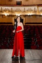 A luxurious actress in a red dress sings on stage with a microphone in her hands