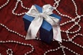 Luxurious blue gift box with a silver ribbon on a red shiny cloth and decorative silver string of pearls. Royalty Free Stock Photo