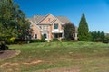 Luxurious brick house with a green lawn and trees at the entrance. Sunny summer day, cloudless sky