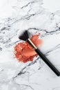 Elegant Makeup Brush Resting on Crushed Coral Blush on a Marble Surface