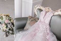 Luxurious pink wedding dress is lying on a grey sofa in a white room. Royalty Free Stock Photo