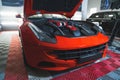 Luxurious red sports car at mechanic's or in car detailing studio parked with open car hood showing deep-cleaned