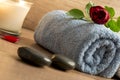 Luxurious wellness arrangement with a rolled blue towel, red rose, burning candle, and two black massage stones