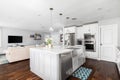 A luxurious white kitchen looking towards a living room.