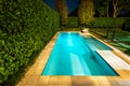 Luxury back yard pool at night in a green landscaped garden surrounded by a hedge and trees Royalty Free Stock Photo