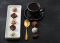 Luxury Chocolate candies in white porcelain plate with cup of black coffee and golden spoon on dark table background Royalty Free Stock Photo