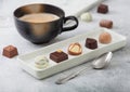 Luxury Chocolate candies in white porcelain plate with cup of cappuccino coffee and silver spoon on light table background Royalty Free Stock Photo