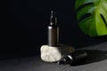 Luxury cosmetics set of black dropper bottles and tropical green leaf on dark background.