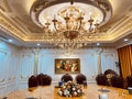 Luxury dining room interior with many shiny gold-plated details, crystal chandeliers, wooden chairs, and classic wall painting