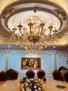 Luxury dining room interior with many shiny gold-plated details, crystal chandeliers, wooden chairs, and classic wall painting