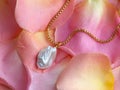 Luxury elegant baroque pearl pendant with golden chain on pink yellow rose petals Royalty Free Stock Photo