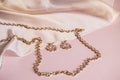 Luxury gold jewelry chain and earrings on pink background with silk, copy space, selective focus Royalty Free Stock Photo