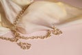 Luxury gold jewelry chain and earrings on pink background with silk, copy space, selective focus Royalty Free Stock Photo