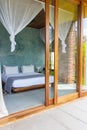 Luxury hotel room with mosquito net and open doorway. Comfortable interior of tropical hotel. Cozy and elegant bedroom design.